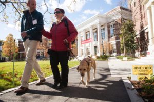 A human guide and a service dog walking with a blind woman