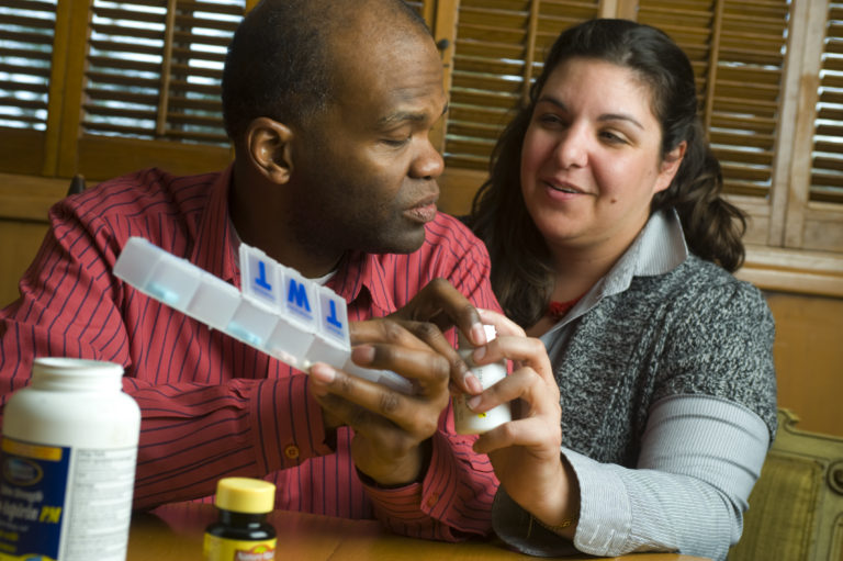 Volunteer showing a blind man how to use a pill box.