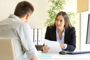 Woman holding a piece of paper sitting at a desk talking to a man