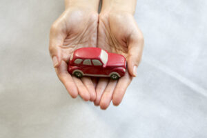 Red toy car being help by two outstreched hands