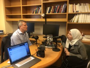 Randy Cohen Sitting behind desk , woman wearing a hajib in front speaking into microphone