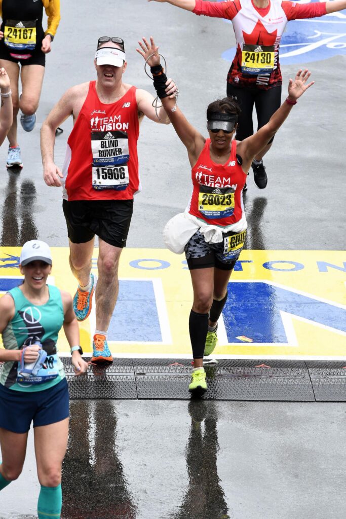 Two Team With A Vision runners crossing the Boston Marathon finish line.