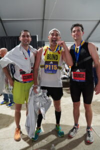 TWAV runner Joe Burket with his two guides holding up their medals at the end of the race