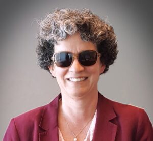 Headshot of Jennifer Harnish, PhD. Jennifer is wearing a professional jacket with a white shirt and necklace. She wear darkened glasses and has salt and pepper colored hair. She is smiling.