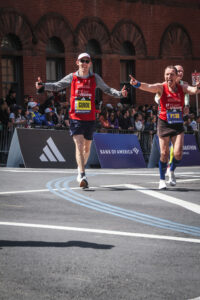 Two Team With A Vision runners run the Boston marathon and they each give double thumbs up and smile